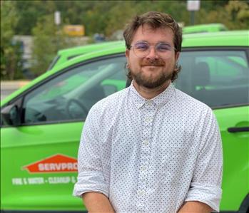 Male employee smiling in front of green trucks and wearing glasses